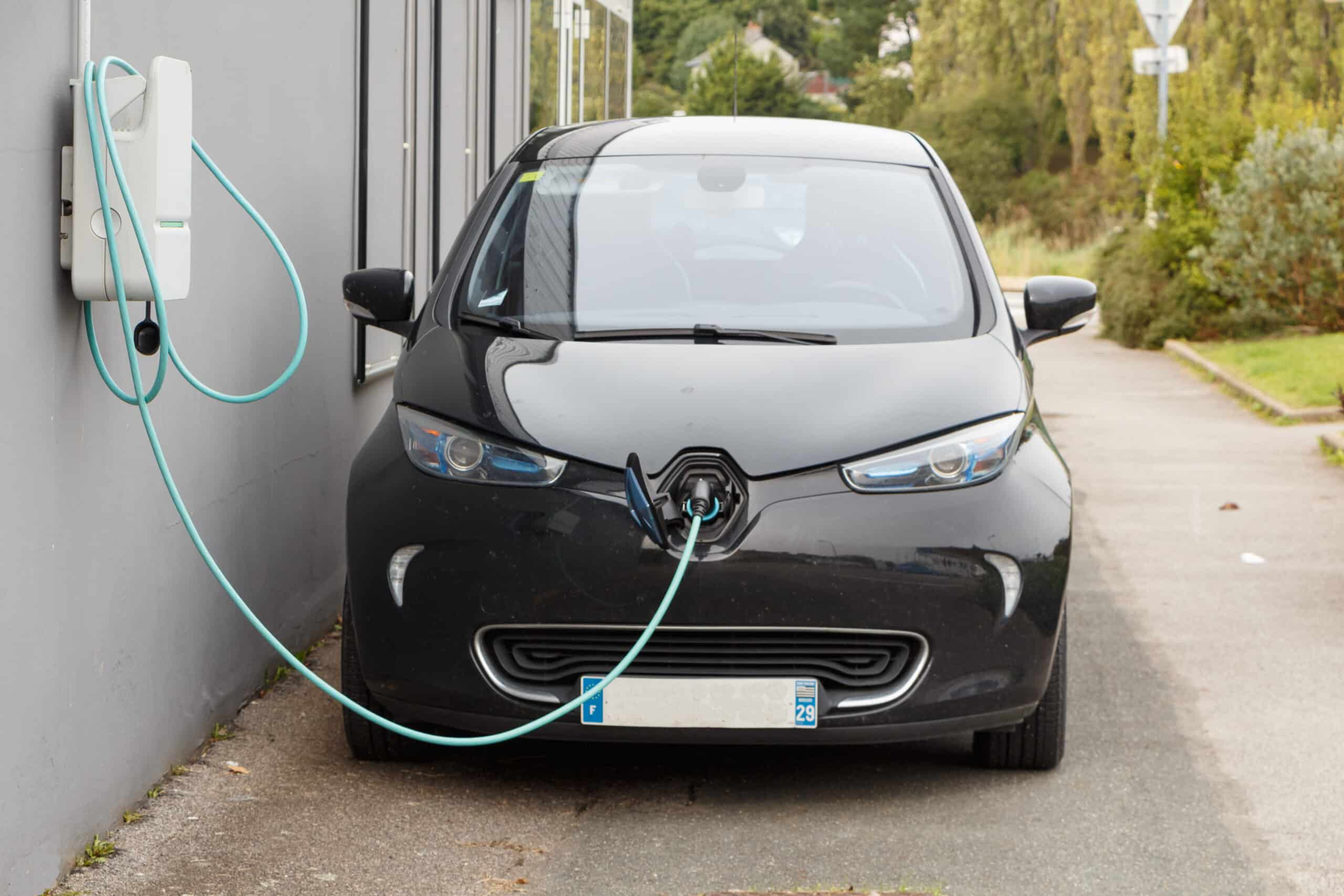 Voiture électrique noire Renault Zoé branchée à une borne de recharge murale grise avec un câble bleu. Plaque française "F" "29".