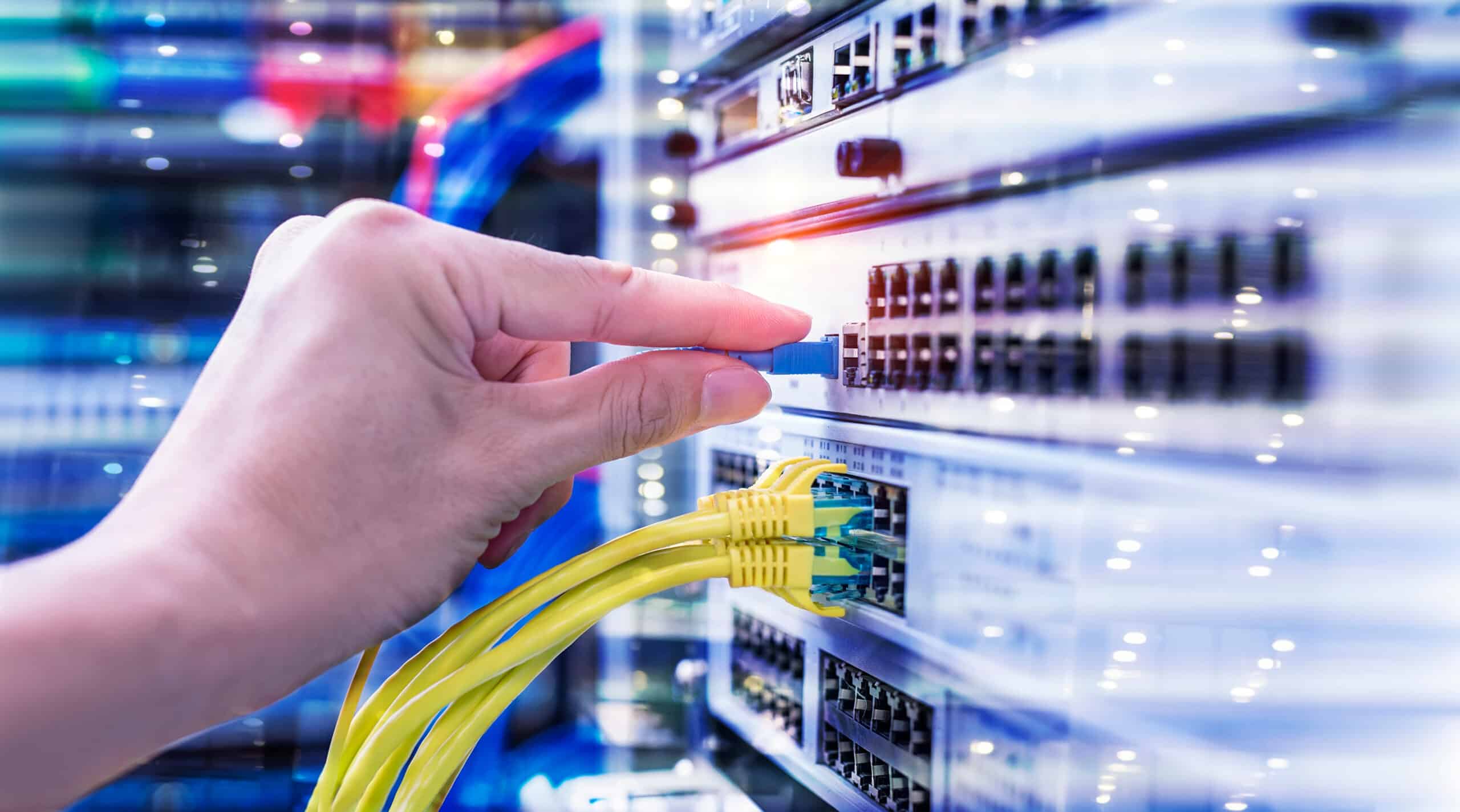 Main branchant un câble de fibre optique bleu dans un commutateur réseau. Des câbles Ethernet jaunes sont déjà connectés.