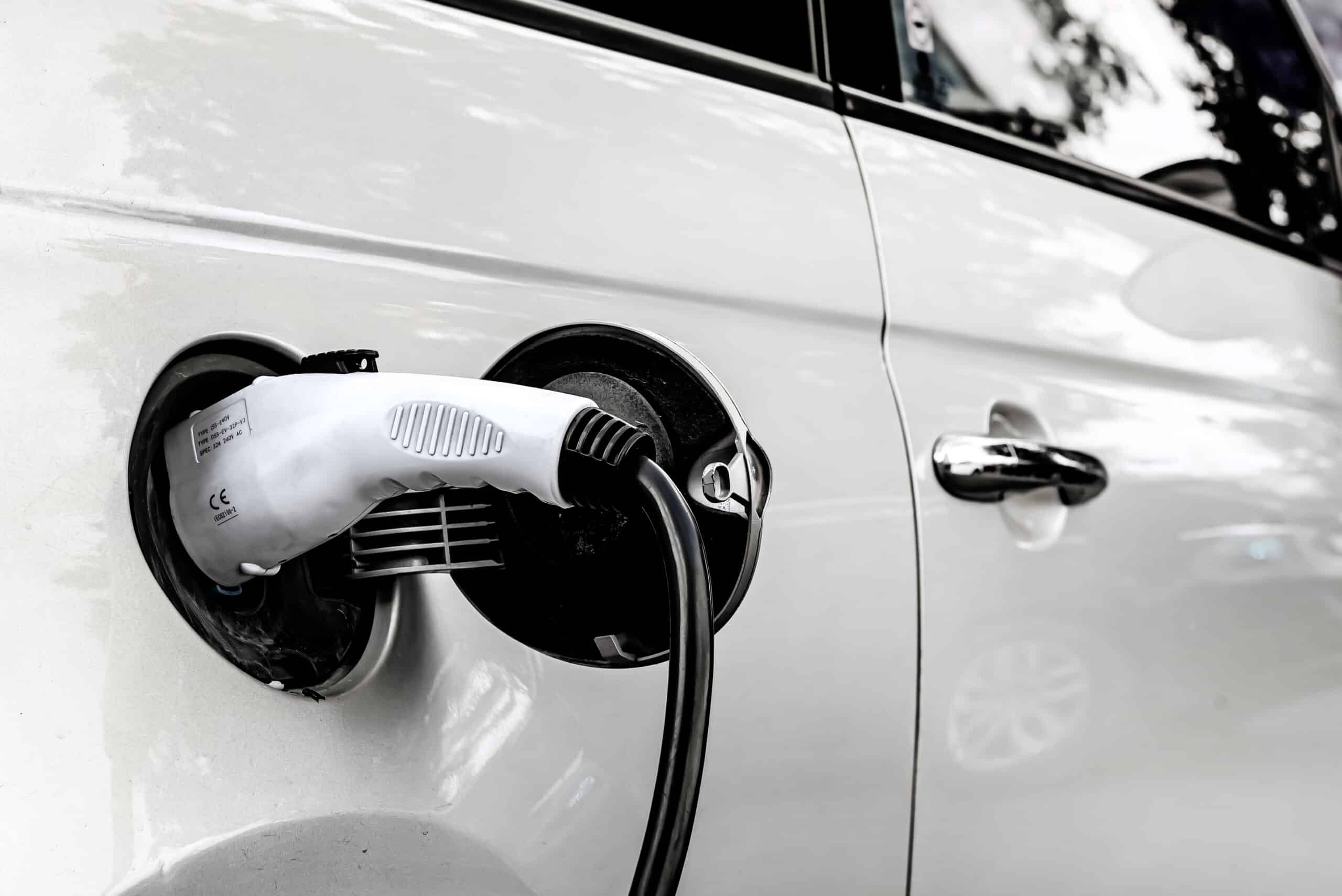 Câble blanc et noir branché sur le port de charge ouvert d'une voiture électrique blanche. Texte sur le chargeur: CE, 32A 240V AC, IEC62196-2.
