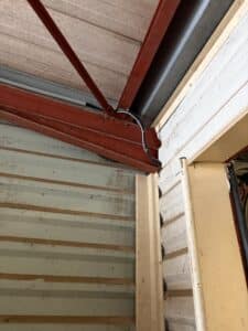 Charpente rouge et câbles fixés dans un hangar avec bardage métallique et structure industrielle.