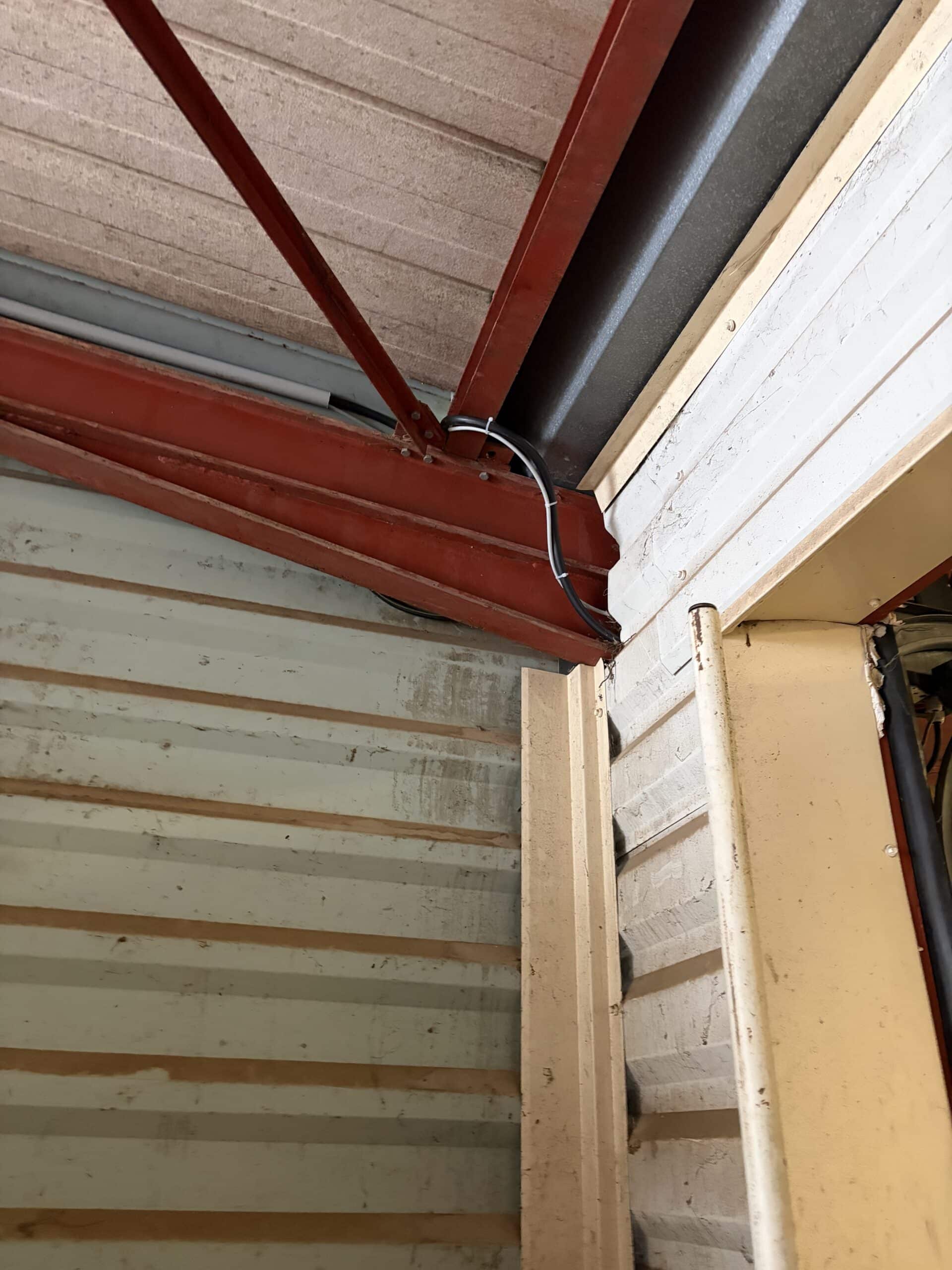Charpente rouge et câbles fixés dans un hangar avec bardage métallique et structure industrielle.
