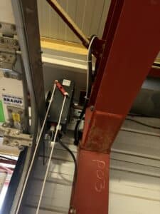 Moteur de porte Fermetures Métalliques Brajus avec système de débrayage manuel rouge et câblage sur structure.