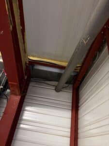 Poutre en acier rouge marquée PO3, tuyau PVC gris et panneaux blancs ondulés dans une structure industrielle.