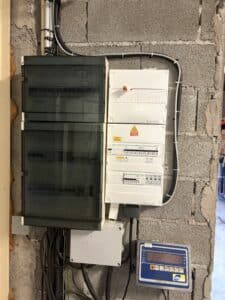 Tableaux électriques Schneider, boîtier coupure photovoltaïque et afficheur de balance sur un mur en parpaing.
